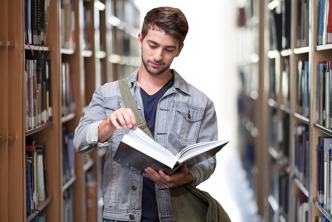 Jeune homme qui feuillette un livre dans une bibliothèque